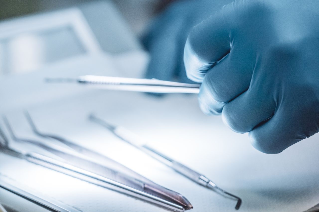 Close-up of a surgeon's gloved hand holding surgical instruments in a sterile setting.