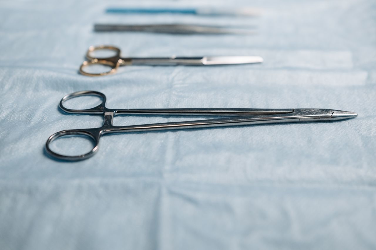 Close-up of surgical tools including a needle holder on a blue cloth in a medical setting.