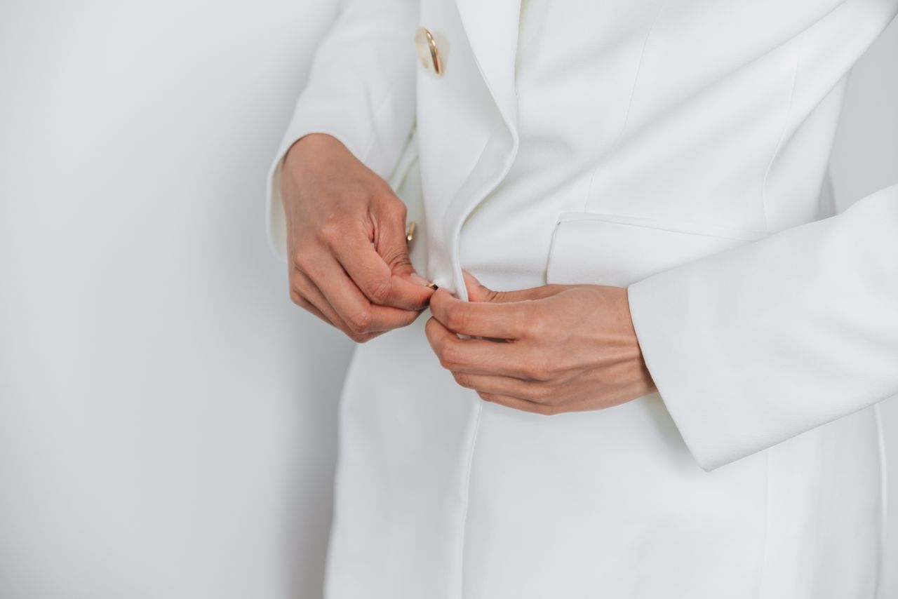 Close-up of adult hands buttoning a white coat, showcasing elegance and style.